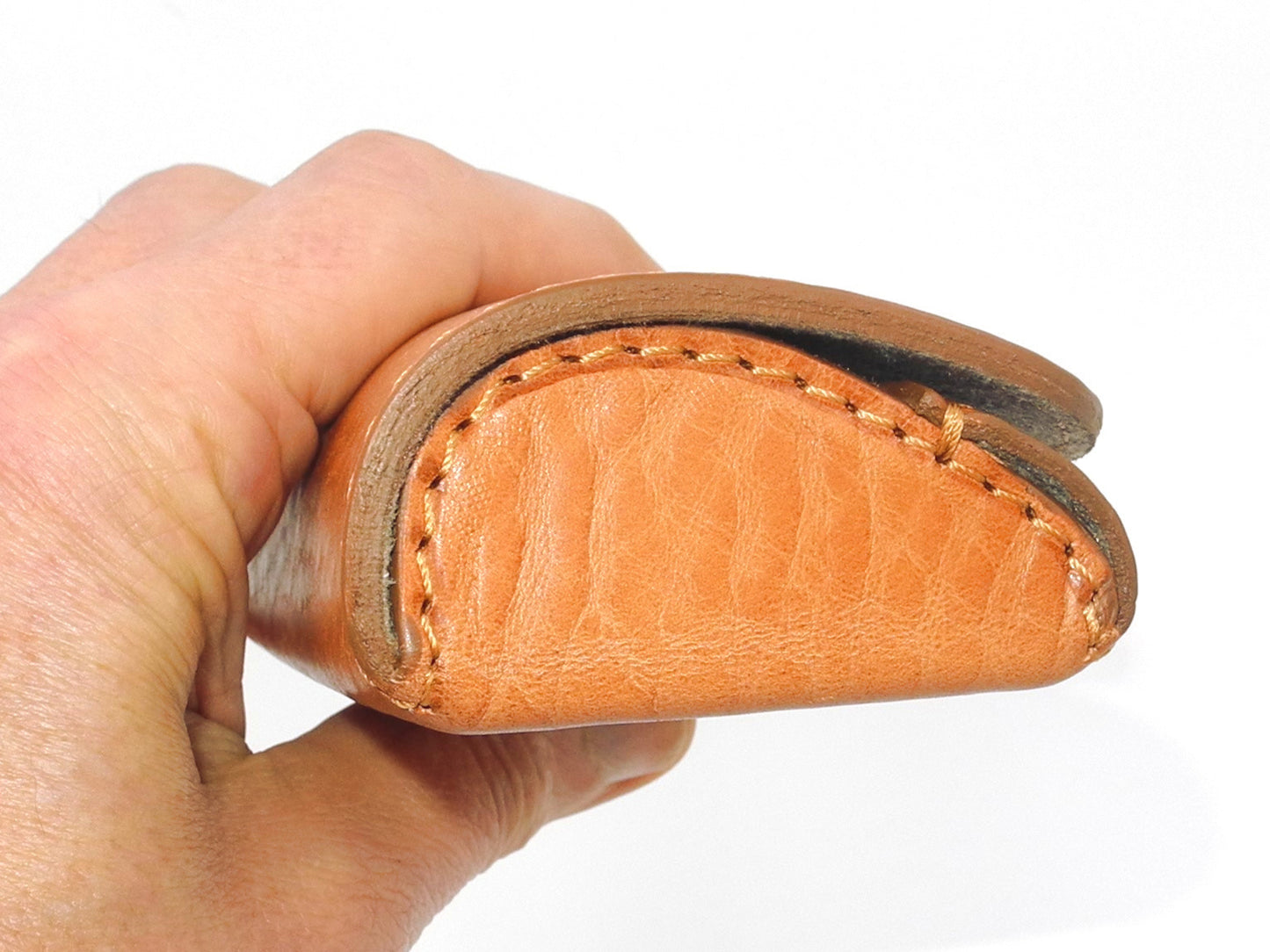 A light brown leather eyeglass case, viewed from the side and held in a hand to show the size.
